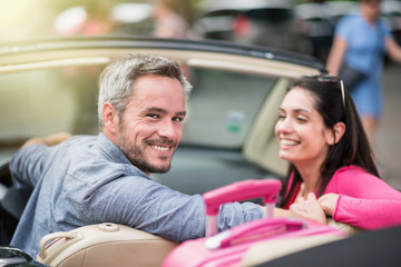 cheerful couple going on a road trip in their convertible car - obrazy, fototapety, plakaty