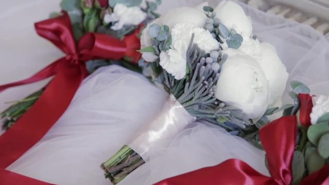 A wedding bouquet of beautiful white peons is lying on the white veil material by other two bouquets. Portrait. No people around. Inside shooting. Wedding atmosphere. Camera stabilizer, close up view.