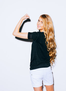 Young beauty fitness sexy blonde woman showing her muscles, her back to the camera, long hair and smiling. Indoor. Warm color.