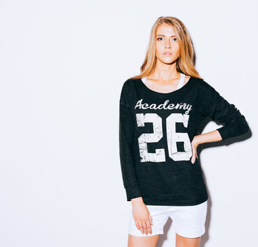 Very beautiful girl with long blond hair posing on a white background. Sweatshirt and white shorts. Indoor. Warm color.