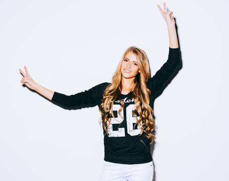 Funny lifestyle portrait of crazy girl, emotional and happy mood, having fun, chic clothes. Shows sign Victory. Spread her arms . Indoors. Warm color.