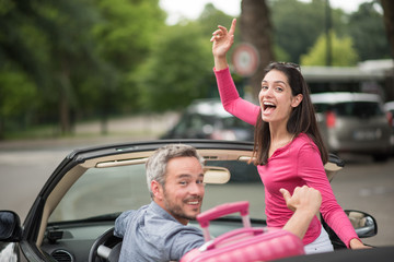 cheerful couple going on a road trip in their convertible car