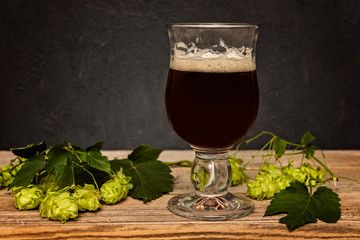Glass of dark  beer and hop cones on wooden table