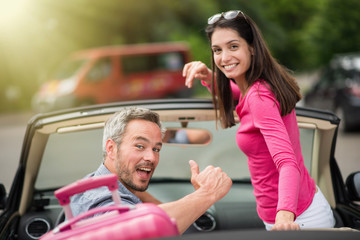 cheerful couple going on a road trip in their convertible car