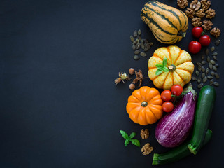 Pumpkins, eggplant, zucchini, cherry tomatos, pumpkin seeds, nuts and basil on black background, overhead shot, corner frame