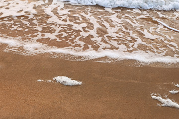 Sea wave over sand with foam on its top