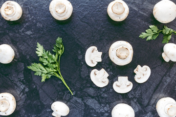 Fototapeta na wymiar Top view of fresh mushrooms champignons and parsley on black table