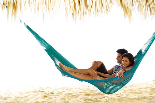 This Young Couple Relax In A Hammock On Vacation, Under A Palapa, Cabana On The Beach In Central America