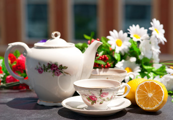 Чай в изящном чайном сервизе, лимон и цветы на балконе под лучами солнца.