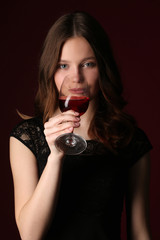 Girl drinking wine. Close up. Dark red background