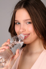 Girl in pink top drinking water. Close up. Gray background