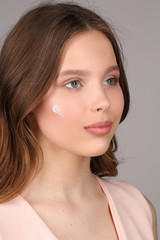 Obraz premium Girl in pink shirt with cream on her face. Close up. Gray background