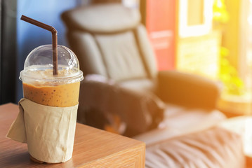 Cold coffee with straw in plastic cup on brown wooden table