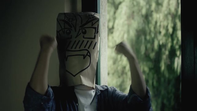 A furious revengeful breadbag face near a window on a rainy day, throwing a tantrum, coming close to the viewer, covering the camera. Close-up shot.
