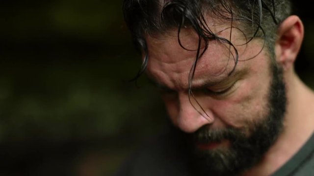 A man glances down (at an unseen compass) and around at his surroundings in a forest.