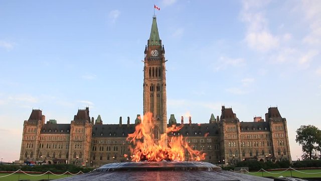 Centennial Flame burning brightly in front of Peace Tower and Centre Block on Parliament Hill, Ottawa, Canada. Parliament Building was lit by morning sun light under blue sky and white clouds