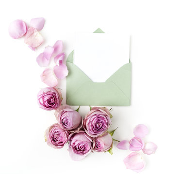 Paper envelop with white card and pink roses. Flat lay, top view