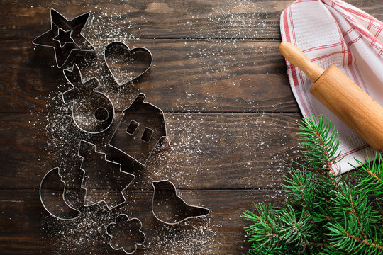 Christmas background with cookies cutters, flour, spices and green fir branches on old rustic wooden table, top view