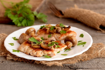 Fried Turkey breasts with grated cheese, mushrooms and parsley on a plate and on a burlap. Fresh parsley, cutlery on a wooden table. Tasty to cook Turkey breasts. Vintage style. Macro 