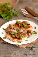 Fried Turkey breasts with grated cheese, mushrooms and parsley on a plate and on a burlap. Fresh parsley, cutlery on a wooden table. Delicious to cook Turkey meat. Vintage style. Macro  