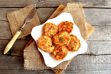 Fried fish cakes on a plate, fork on old wooden background. Cutlets from minced salmon. Delicious and nutritious lunch or dinner