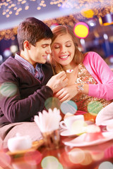 Young man feeding his girlfriend with cake in cafe