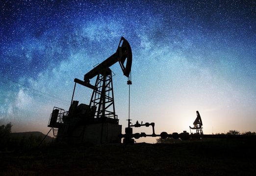 Silhouette of two oil pumps are working on the oil field in the evening under night sky with stars. Oil industry equipment. Milky way shines above