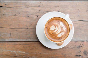 Hot cappuccino in black ceramic cup with beautiful latte art on wooden table.
