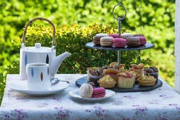 Rolgordijnen Tea with cakes and macaroons set up in the garden © beataaldridge