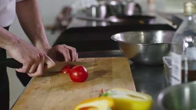 Closeup of male hands cutting tomatoes on wooden board and then putting it into metal bowl