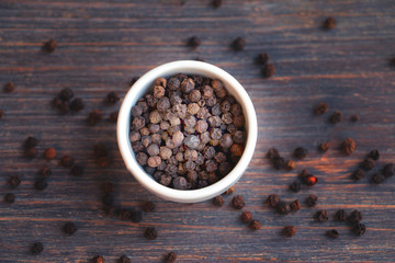 Black pepper  bowl and on wooden table. Selective focus, special light, toned image. Top view. Copy space.