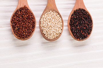 Red, black and white quinoa seeds on a wooden background