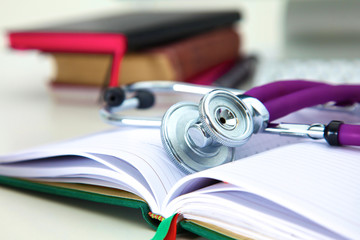 Stethoscope lying on a notebook computer in the background and books