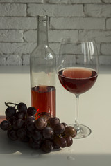 Rose wine in a glass, grapes and wine bottle on the table. Bright brick wall.