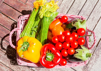 Zucchine, melanzane, peperoni e pomodori in un cestino sopra a una tavola di legno. Cucinare con ortaggi e verdure