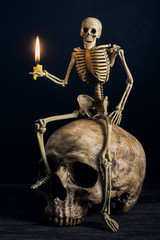 skeleton sitting on big skull with burning candle in hand
