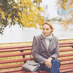 Fototapeta premium Young woman in grey coat sitting on a bench