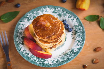 Pancakes with caramel apples, fresh peaches, blueberries and almonds on a colorful vintage plate. Healthy sweet breakfast. Vertical, toned image