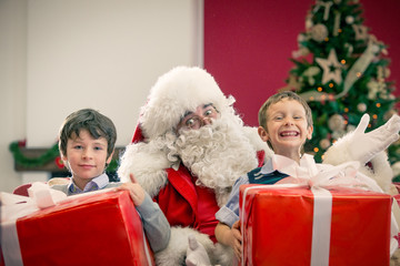Fototapeta na wymiar Santa Claus sitting between two smiling boy with big present at home