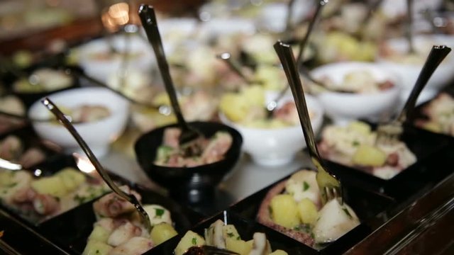 Antipasto di pesce con polipo e patate al cucchiaio dentro ciotole di plastica nere e bianche servite a un buffet di un matrimonio