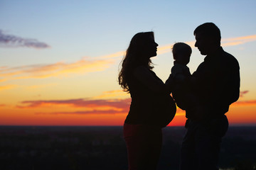 silhouettes of father and son and a pregnant mom at sunset