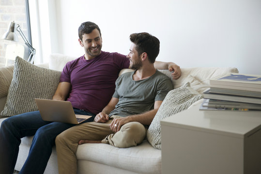 Gay Male Couple Sitting On Sofa At Home Using Laptop