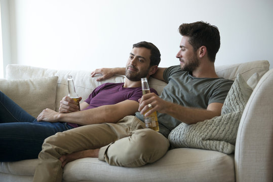 Gay Male Couple On Sofa At Home Watching TV Drinking Beer