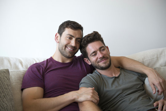 Gay Male Couple On Sofa At Home Watching TV 