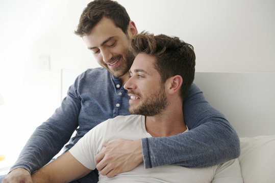 Gay Male Couple At Home Relaxing In Bed Together