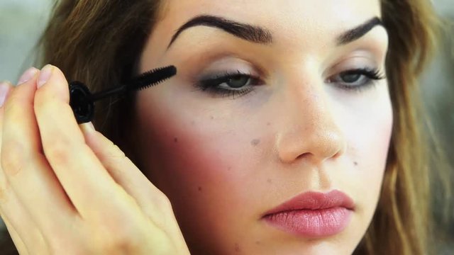 Young model applying eyelash near mirror