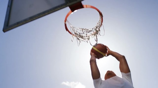 Basketball player slam dunking on a hoop outdoors, in slow motion