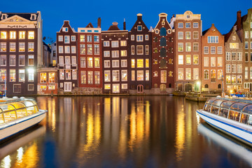 Naklejka premium Beautiful typical Dutch dancing houses at the Amsterdam canal Damrak at night, Holland, Netherlands.