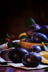 Blue plums with leaves. Wooden bowl with fruit. Rustic style, lo