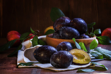 Blue plums with leaves. Wooden bowl with fruit. Rustic style, lo